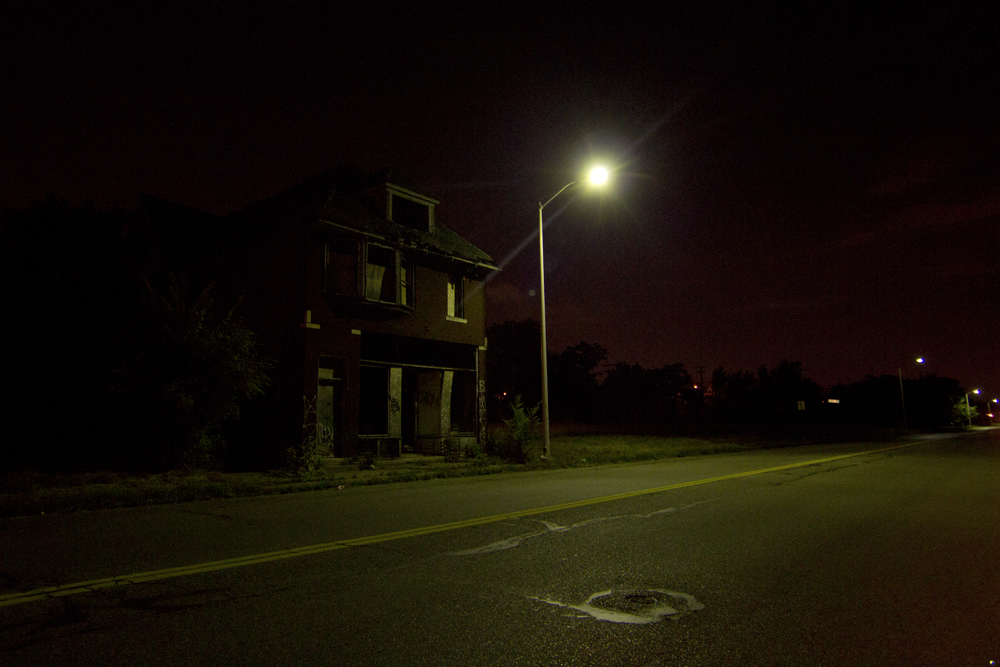 A working streetlight illuminates an abandoned house. 